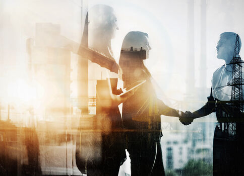 Zwei silhouettes Geschäftspersonen schütteln sich die Hände vor einer industriellen Kulisse mit Gebäuden und Kraftwerken; die Szene symbolisiert Zusammenarbeit und eine geschäftliche Vereinbarung.