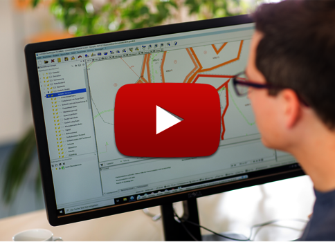 Eine Person mit Brille sitzt vor einem Monitor, der eine Kartensoftware mit detailreicher Straßenkarte zeigt; ein großes rotes Play-Symbol überlagert das Display.