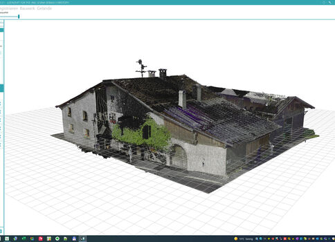 Maquette 3D d'une maison ancienne, toit à deux pentes et tuiles sombres, murs en pierre et enduit, avec porche et entrée arquée. Un arbre se dresse devant, sur une grille de référence dans une interface de modélisation 3D.