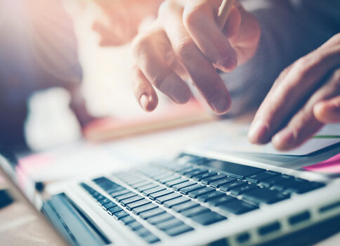 Nahaufnahme: Eine Person tippt auf der Laptop-Tastatur; Hände bewegen sich über die Tasten, während warmes Licht ins Bild fällt.