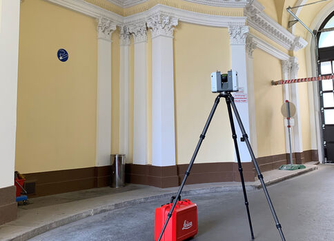 Historischer Innenraum mit gelben Wänden und weißen Säulen. Vor einem Stativ mit Messgerät steht eine rote Transportbox; im Hintergrund rechts ist eine Absperrung und ein Fenster sichtbar.