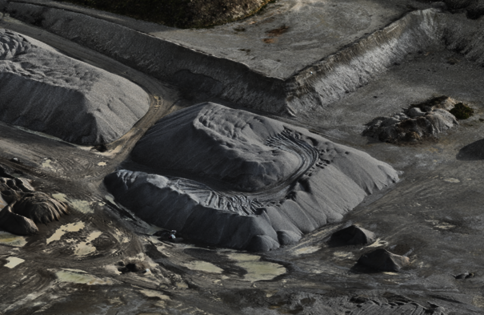 Graue geologische Landschaft mit großen, runden Erhebungen aus Vulkanmaterial. Die umliegenden Flächen sind flach und dunkel mit Rinnen und gestuften Formen, sichtbar geformt durch erstarrte Lava oder Schlammströme.