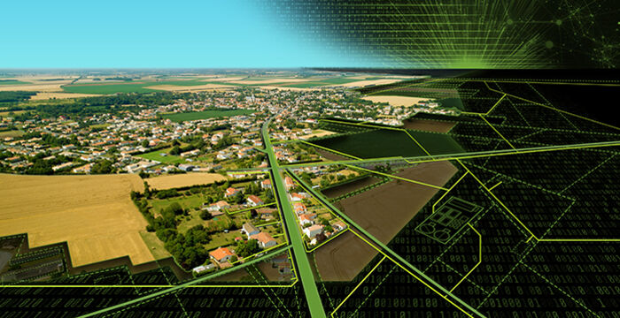Luftaufnahme einer ländlichen Landschaft: weite Felder, ein Dorf mit Häusern, eine Hauptstraße, die durch das Siedlungsgebiet führt; im Hintergrund offene Felder und grüne Flächen. Der Himmel ist klar blau.