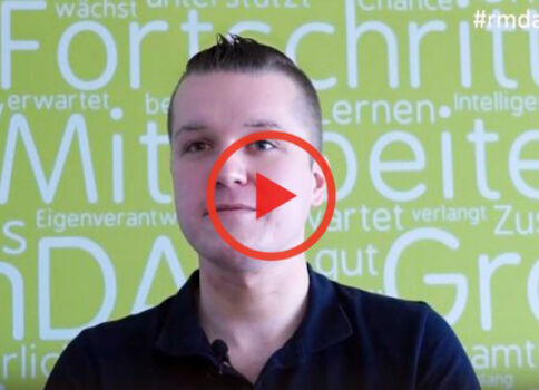 Video-Vorschaubild: Ein Mann blickt in die Kamera, vor grünem Hintergrund; in der Mitte befindet sich ein roter Play-Button.