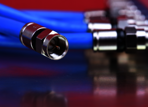 Nahaufnahme eines blauen Kabels mit einem metallischen Steckverbinder im Vordergrund; im Hintergrund liegen weitere silberne Steckverbinder unscharf.