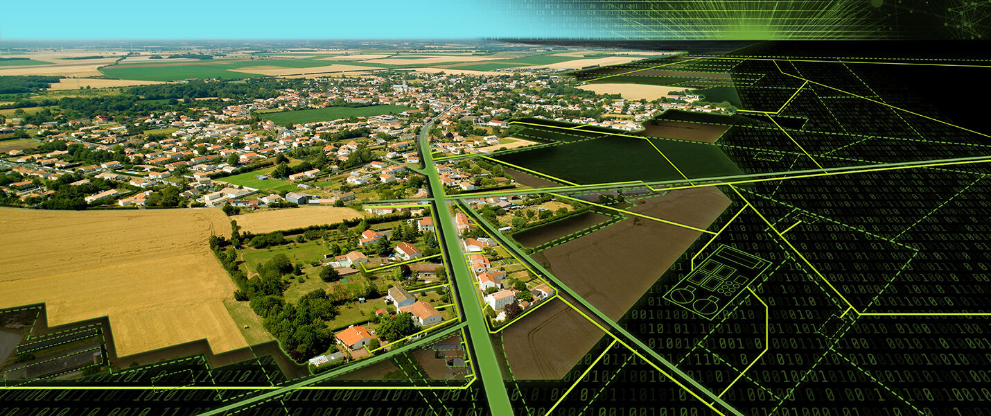 Luftaufnahme eines Dorfes mit einer Hauptstraße, umgeben von Feldern und Einfamilienhäusern; grüne Felder erstrecken sich bis zum Horizont.