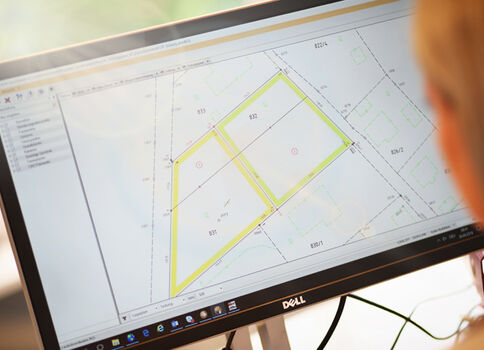 Dell-Monitor zeigt eine CAD-Zeichnung eines Grundstücksplans mit zwei gelb markierten Parzellen; unscharfer Hintergrund.