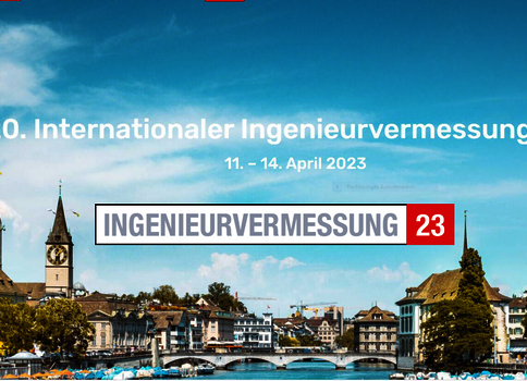 Stadtszene am Fluss mit Brücke; im Vordergrund ein Banner kündigt den 20. Internationalen Ingenieurvermessungskurs an (11.–14. April 2023).