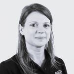 Schwarzweißes Porträt einer jungen Frau: helles, glattes Schulterlanges Haar, schwarze Bluse, große Creolen; leichtes Lächeln, Blick zur Kamera vor hellem Hintergrund.