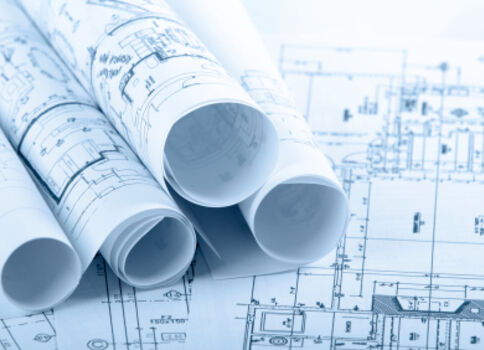 Mehrere eingerollte Architektenpläne liegen auf einem Tisch; blaue Drucke zeigen technische Zeichnungen und Grundrisse.
