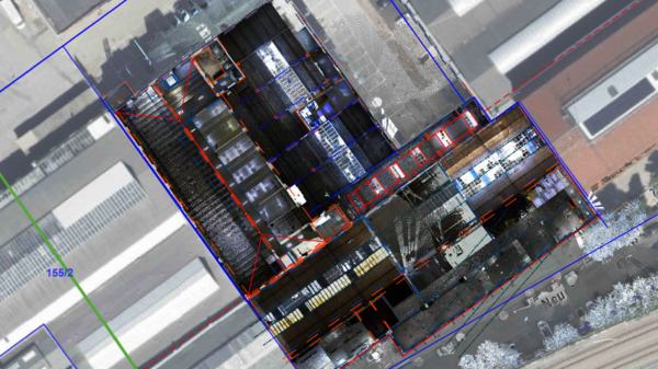 Luftbild eines großen Industrie-Lagerhauses mit freiem Dachbereich: Einblick in das Innenlager mit vielen gestapelten Paletten auf Regalen; umliegende Gebäude und Straßen sind sichtbar.