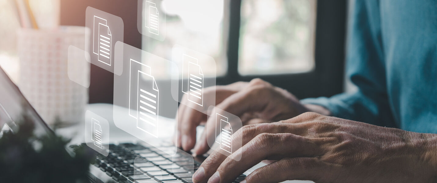Eine Person tippt auf einem Laptop; über der Tastatur schweben transparente Dokumentensymbole, die digitale Dateien repräsentieren, während der Hintergrund unscharf bleibt.