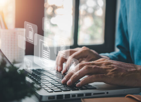 Eine Person tippt auf der Laptop-Tastatur, während über dem Gerät transparente Dateisymbole schweben, die digitale Dokumente oder Dateiübertragung andeuten.
