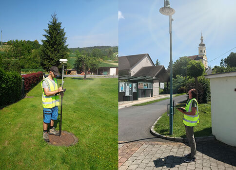 Zwei Personen in fluoreszierenden Sicherheitswesten führen Vermessungsarbeiten im Freien durch. Links steht ein Mann mit Vermessungsgerät auf einem Stativ in der Grasfläche eines Parks; rechts eine Frau an einer Straßenecke neben einer Laterne, ebenfalls mit Messausrüstung.