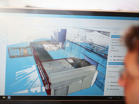 Écran d’ordinateur affichant une maquette 3D d’une installation industrielle ou d’un bâtiment, avec des composants gris et des surfaces bleues, et une interface utilisateur visible sur le côté.