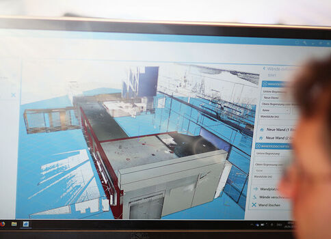 Écran d’ordinateur affichant une maquette 3D d’une installation industrielle ou d’un bâtiment, avec des composants gris et des surfaces bleues, et une interface utilisateur visible sur le côté.