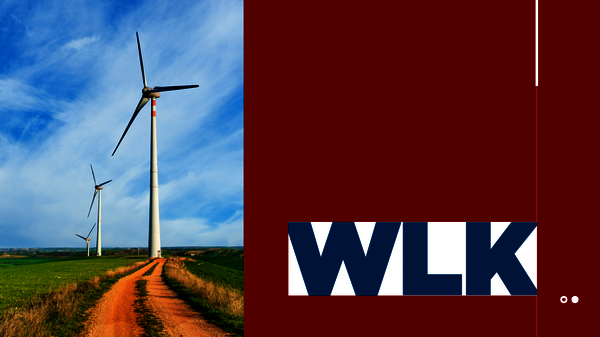 Zwei Windkraftanlagen stehen auf einer grasbewachsenen Landschaft; ein roter Weg führt durch das Feld, während der blaue Himmel Wolken trägt.