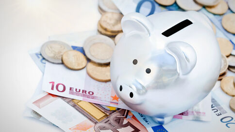 Ein weißes Sparschwein steht auf Euro-Banknoten und Münzen und symbolisiert Sparen.