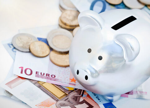 Ein weißes Sparschwein steht auf Euro-Banknoten und Münzen und symbolisiert Sparen.