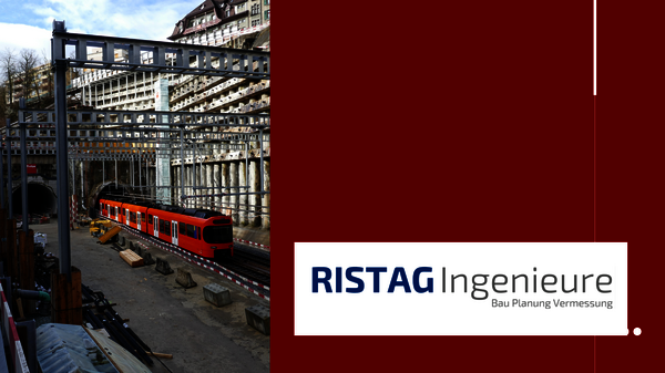 Baustelle mit rotem Zugwagen auf Gleisen, umgeben von Stahlgerüsten, Baumaterialien und Baugeräten; im Hintergrund wird ein mehrstöckiges Gebäude errichtet.