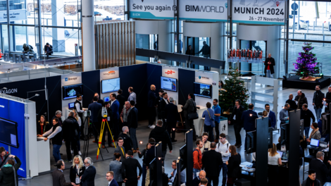Große Messehalle mit vielen Ausstellungsständen und Besuchern, die sich austauschen und Präsentationen ansehen. Überall Monitore an Ständen; Banner weisen auf BIMWORLD MUNICH 2024 hin – eine lebhafte Messeatmosphäre.