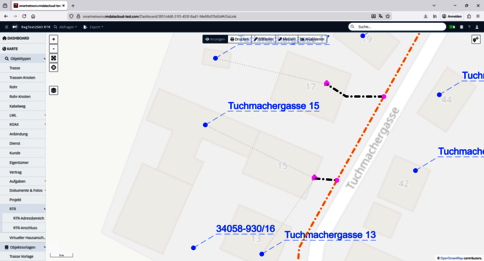 Kartenansicht der Tuchmacherstraße mit Gebäuden und farbigen Markierungen. Blau markierte Punkte verteilen sich entlang der Straße, pinke Marker markieren Standorte. Eine orange gestrichelte Linie verläuft neben der Straße. Sichtbare Adressen: Tuchmacherstraße 13 und 15; Kennziffer 34058-930/16 in der Nähe.