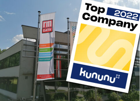 Außenaufnahme eines modernen Bürogebäudes mit zwei Fahnen; eine zeigt das rm DATA-Logo, daneben sind bunte Streifen zu sehen. Über dem Bild liegt ein Kununu-Top-Company-2022-Abzeichen, das eine Auszeichnung als Top-Unternehmen kennzeichnet.