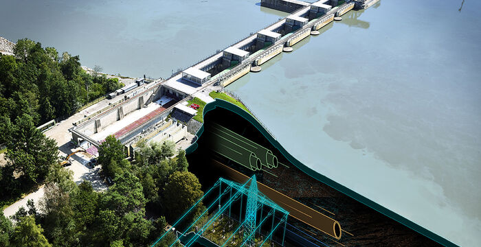 Luftaufnahme eines Staudamms an einem Fluss: eine grün lackierte, bogenförmige Überlaufwehr mit angrenzenden Schleusenbauwerken; Ufer von Wald umgeben, links dicht, rechts hellblaues Wasser.