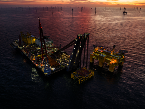 Offshore-Bohrplattform im Meer bei Sonnenuntergang. Gelbe Strukturteile und ein großer Kran ragen aus dem Wasser, Beleuchtung leuchtet. Im Hintergrund sind weitere Ölplattformen und Pfähle zu sehen. Ruhiges Wasser spiegelt den warmen, orangefarbenen Himmel.