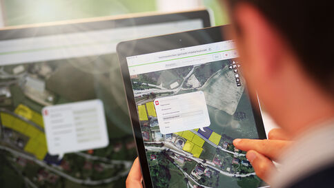 Auf einem Tablet ist eine Kartenansicht mit Satellitenbild zu sehen; über der Karte liegt ein Informationsfenster.