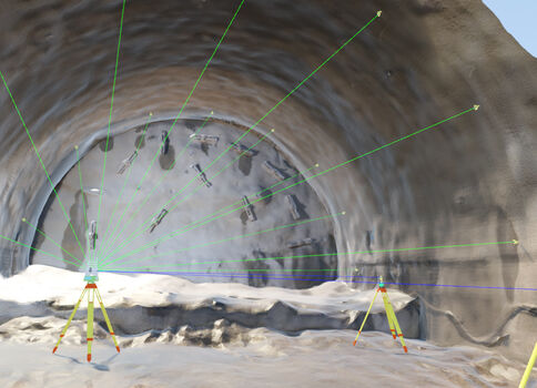 Innenansicht eines Tunnels im Rohbau. Vorne stehen drei Vermessungsstative mit gelb-roten Füßen, aus denen grüne Laserstrahlen durch den Tunnel ziehen und die Felswand ausleuchten.