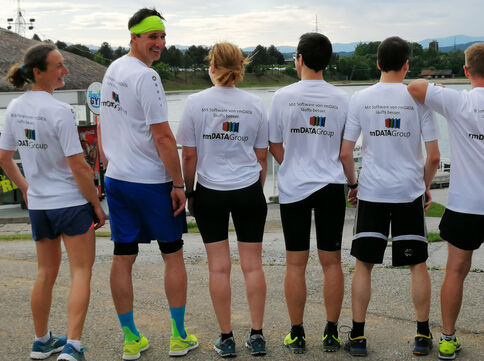 Gruppe von Läufern in weißen T-Shirts mit rmDATAGroup-Logo steht in einer Reihe, von hinten fotografiert, bei einem Outdoor-Laufevent.