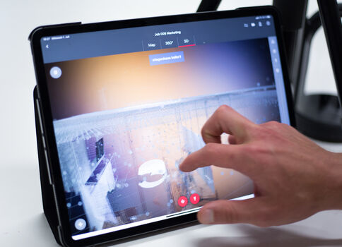 Nahaufnahme: Eine Hand berührt den Bildschirm eines Tablets, auf dem eine Live-Videoansicht sichtbar ist.