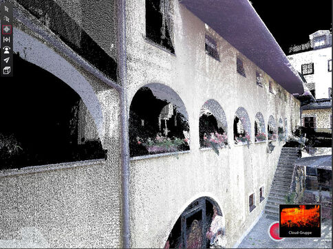 Außenansicht eines mehrstöckigen Gebäudes mit einer Reihe halbrunder Arkaden im Erdgeschoss; hinter den Bögen sind Fenster und Blumenkästen sichtbar. Eine Treppe rechts führt zu einer oberen Ebene.