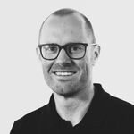 Schwarz-weißes Porträt eines lächelnden Mannes mit Brille und dunklem Hemd.