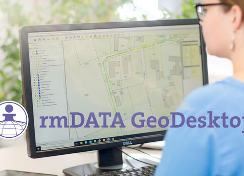 Eine Person sitzt mit dem Rücken zum Betrachter vor einem Monitor, auf dem eine Geoinformationskarte (GIS-Ansicht) angezeigt wird; das rmDATA GeoDesktop-Logo ist sichtbar.