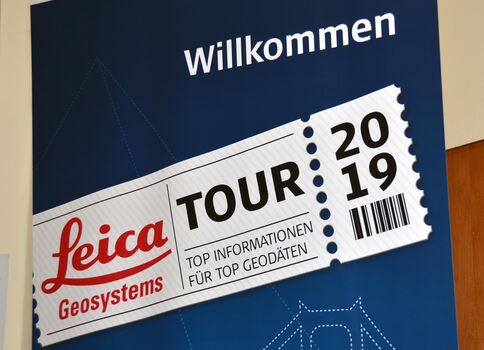Blaues Willkommensbanner mit einem Leica Geosystems Tour-Ausweis-Design: Leica-Geosystems-Logo, der Schriftzug TOUR, die Jahreszahl 2019 und ein Barcode.