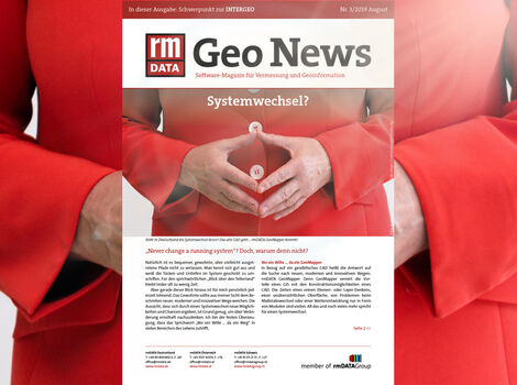 Eine Person in rotem Mantel formt mit beiden Händen ein Herz über dem Bauch; dahinter ein Magazincover mit der Aufschrift Geo News und dem Titel Systemwechsel?