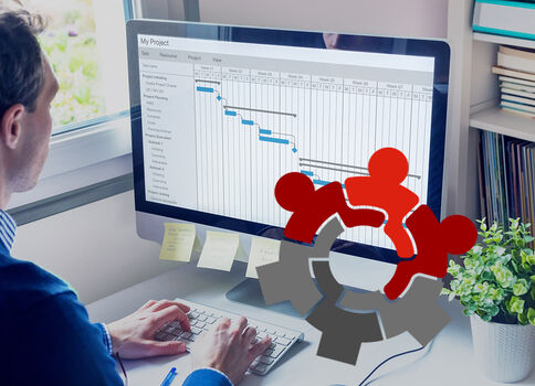 Eine Person sitzt an einem Schreibtisch und arbeitet am Computer. Auf dem Monitor ist ein Projektplan in Form eines Gantt-Diagramms sichtbar.