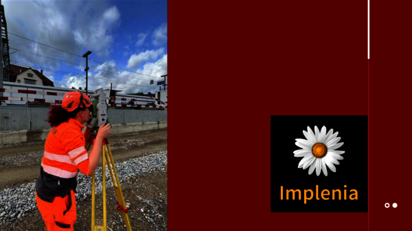 A surveyor in bright orange safety gear and helmet adjusts a tripod-mounted instrument beside railway tracks, with industrial buildings and a blue sky in the background. On the right, a dark panel displays a white daisy logo and the word Implenia.