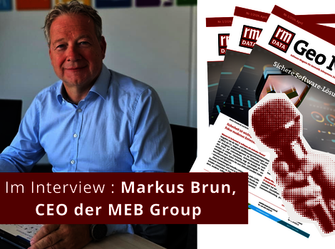 Ein Mann in einem hellblauen Hemd sitzt an einem Schreibtisch in einem Büro; er wird interviewt. Im Vordergrund ein roter Banner mit der Aufschrift 'Im Interview'. Im Hintergrund liegen Magazine.