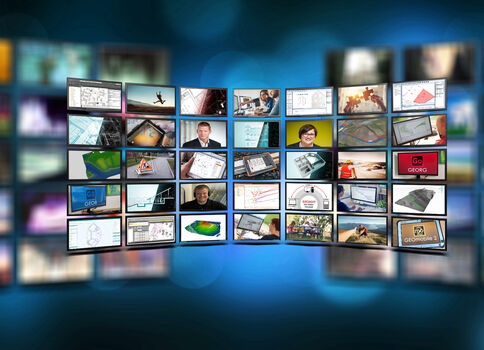 Viele kleine Bildschirme bilden eine gebogene Wand vor blauem Hintergrund und zeigen unterschiedliche Inhalte wie Diagramme, Karten, Computer-Bildschirme, Menschen in Geschäftsumgebungen, Videos und Grafiken – eine Perspektive auf digitale Medien.