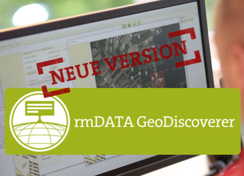 Ein Computerbildschirm zeigt eine Kartenansicht; überlagert ist ein roter Stempel mit 'NEUE VERSION'. Im Vordergrund ein grünliches Banner mit dem rmDATA GeoDiscoverer-Logo und dem Text 'rmDATA GeoDiscoverer'.