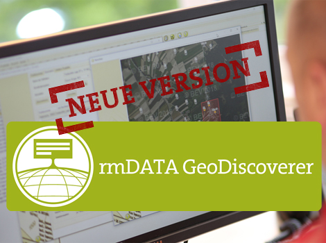 Ein Computerbildschirm zeigt eine Kartenansicht; überlagert ist ein roter Stempel mit 'NEUE VERSION'. Im Vordergrund ein grünliches Banner mit dem rmDATA GeoDiscoverer-Logo und dem Text 'rmDATA GeoDiscoverer'.