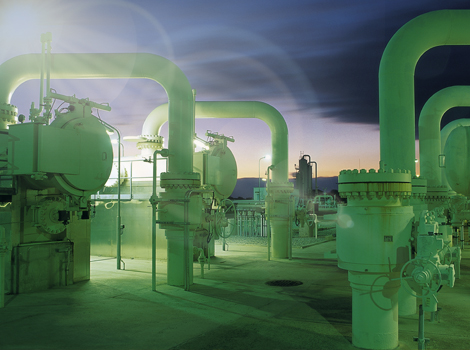 Außenansicht einer Industrieanlage mit großen grünen Rohrleitungen, Tanks und Ventilen auf einer Plattform; der Abendhimmel ist im Hintergrund sichtbar.