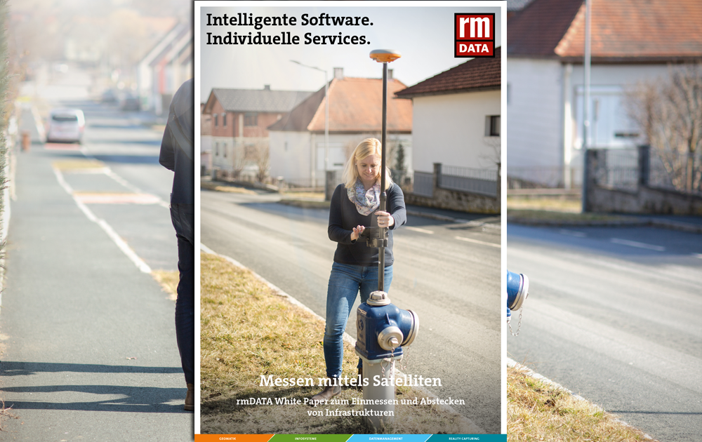 Ein Werbebanner einer IT-Firma steht vor einer Straßenszene; eine Frau hält ein Vermessungsgerät vor sich. Auf dem Banner stehen die Slogans: "Intelligente Software. Individuelle Services." und "Messen mittels Satelliten".